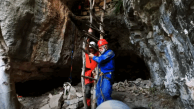 Two cave scientists at the entrance of a cave handing a makeshift ladder